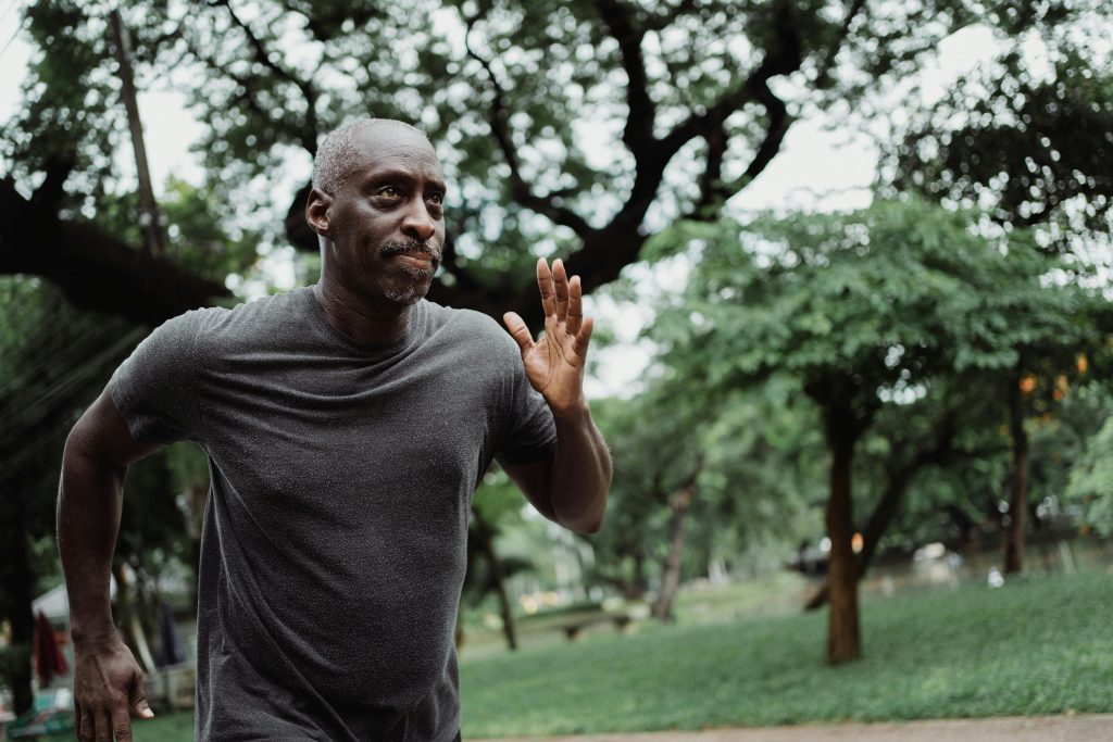 Senior man running through a lush green park, focused on fitness and wellbeing outdoors.